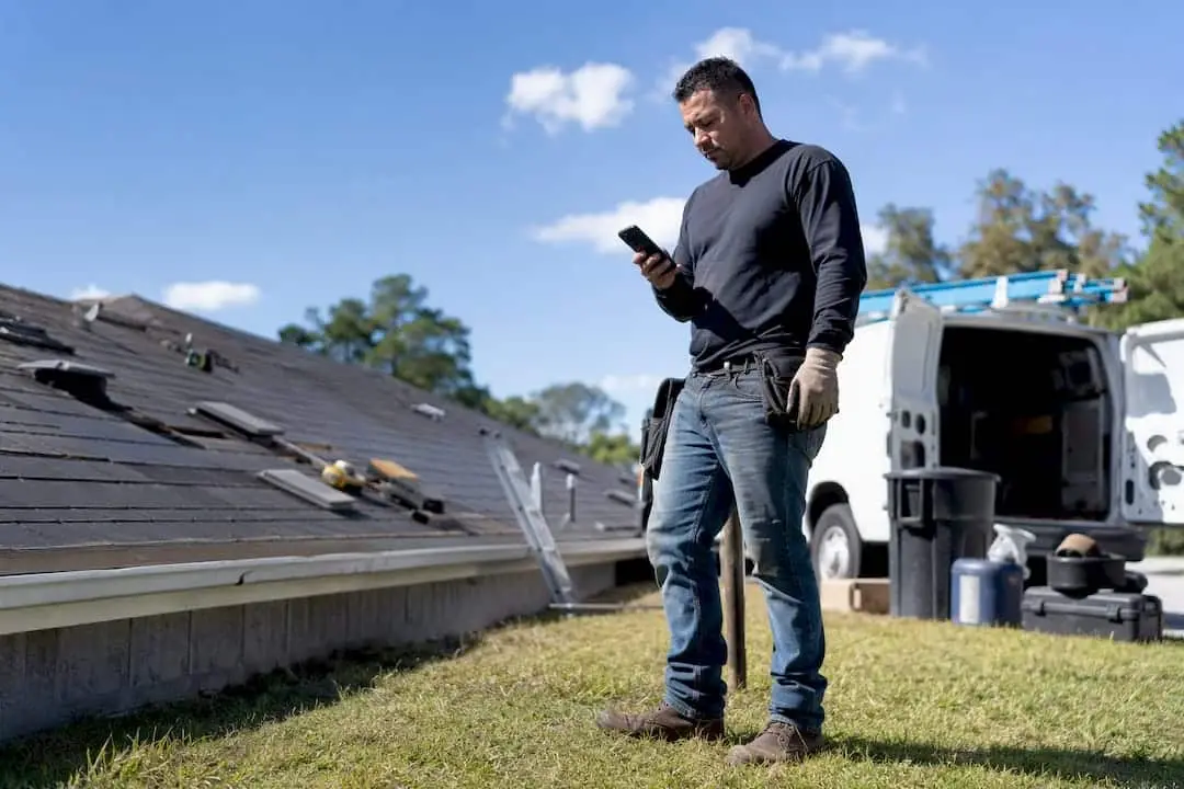 Roofing contractor’s hands holding phone outdoors