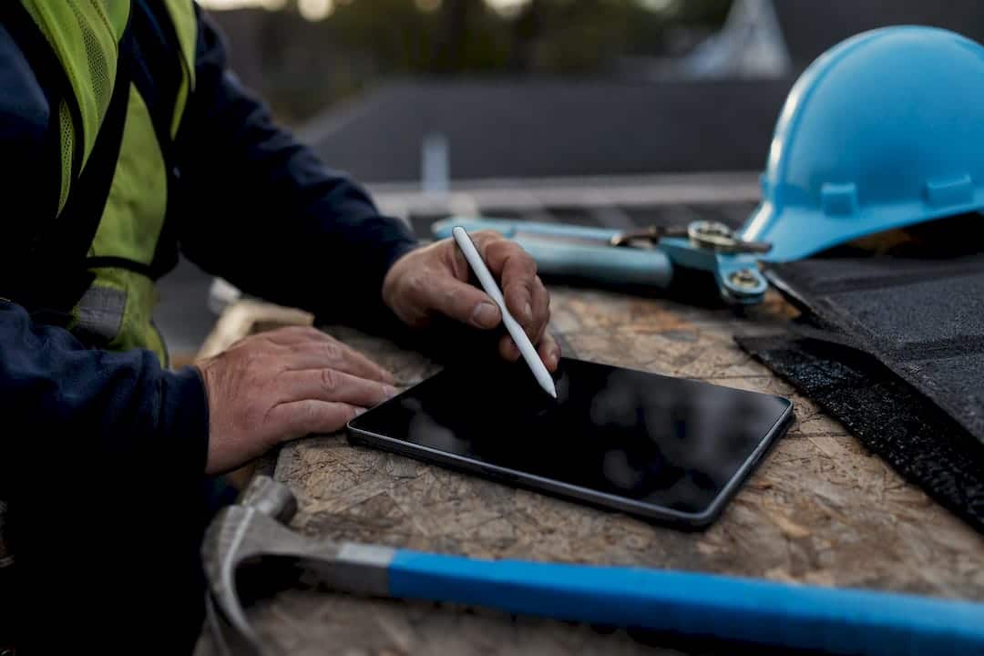 Contractor hands with stylus near dark tablet and tools
